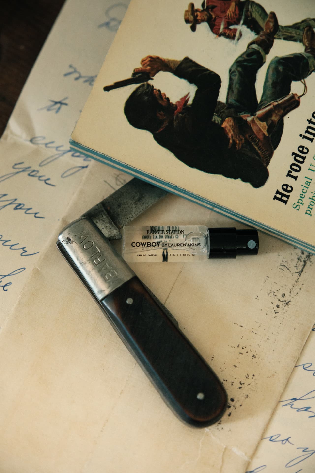 A Cowboy sample vial on a handwritten letter beside a folding knife and a vintage paperback